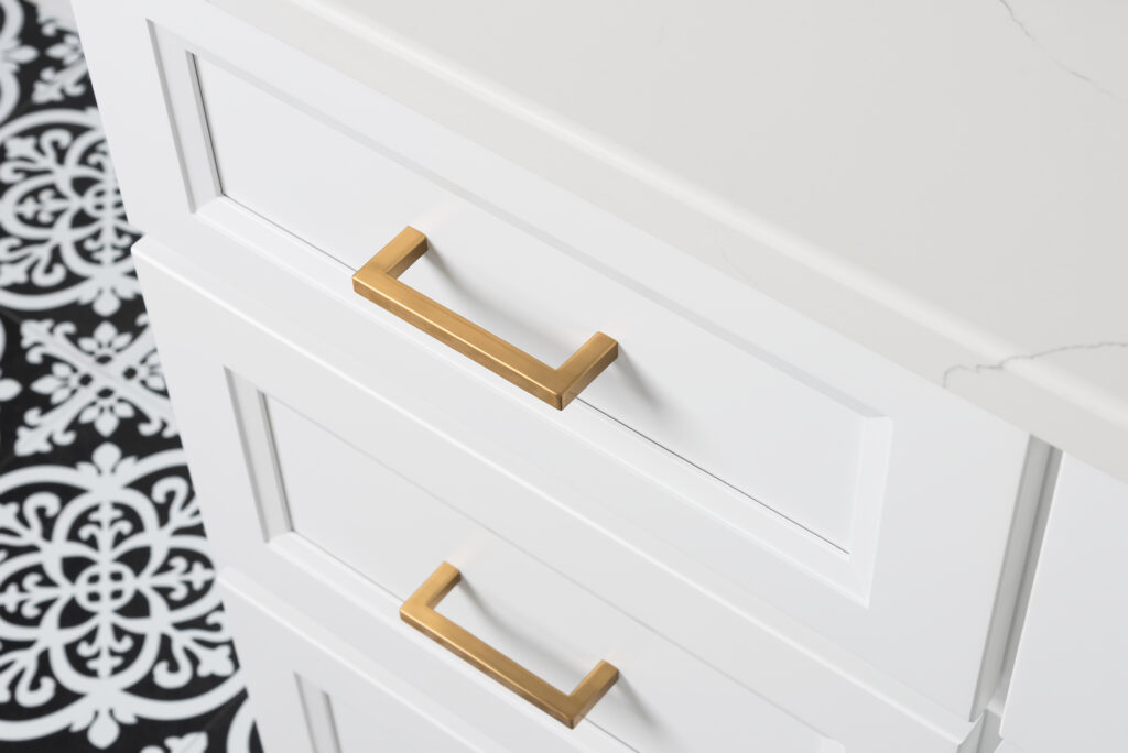 A white dresser with gold handles on a black and white tiled floor.